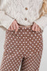 A close-up of a woman wearing brown pants with a white polka dot pattern and two patch pockets, paired with a cream-colored knit cardigan.