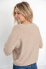 A woman with blonde hair is shown from the back wearing a light beige knit sweater and blue jeans.
