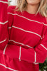A close-up of a woman wearing a bright red knit sweater with horizontal cream-colored textured wavy stripes.