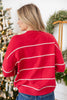 A woman viewed from behind wearing a red knit sweater with horizontal white scalloped stripes, paired with blue jeans.