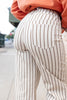 Close-up butt view of a woman wearing brown pinstriped cream pants and an orange sweatshirt, standing outdoors on a sidewalk.