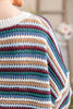 Close-up of a person wearing a chunky knit sweater with horizontal stripes in cream, light blue, teal, burgundy, and tan.