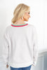 A woman shown from the back wearing a white crewneck sweater with a red and green striped trim, paired with blue jeans.