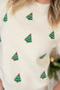 A close-up of a cream knit sweater with small green Christmas tree motifs and red star accents.