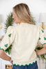 A woman wearing a cream-colored knit sweater with green Christmas tree patterns on the sleeves and hem.