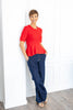 A woman wearing a bright red short-sleeve peplum top and navy blue denim pinstriped trousers.