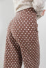 Close-up of a woman wearing brown pants with a white polka dot pattern, paired with a cream knit sweater, against a light gray background.