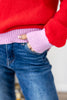 Close-up of a person wearing a bright red knit sweater with a light pink ribbed hem and matching pink ribbed cuffs, paired with blue jeans.