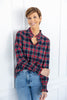 A woman wearing a long-sleeve button-up plaid shirt in navy, red, and white, paired with blue jeans.