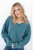 A woman wearing a faded teal blue oversized V-neck sweatshirt and blue jeans.