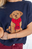 A close-up of a woman wearing a navy blue knit sweater featuring a large knitted puppy wearing a red scarf on the front.