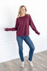 A woman wearing a long-sleeve waffle knit sweater in a maroon color, paired with blue jeans.