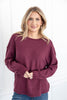 A woman wearing a long-sleeve waffle knit sweater in a maroon color, paired with blue jeans.
