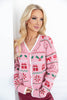 A blonde woman wearing a pink knit cardigan with a festive Christmas pattern of red gifts, green holly, and candy canes, paired with burgundy pants.
