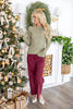 A woman wearing an olive green knit sweater and burgundy wide-leg pants with white pointed flats.