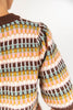 Close-up of a woman wearing a knit sweater with horizontal stripes in brown, cream, pink, yellow, and sage photographed against a plain light background.