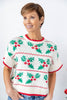 A woman wearing a short-sleeve knit sweater with a Christmas holly and berry pattern in green, red, and white.