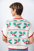 A woman viewed from the back wearing a short-sleeve knit sweater with a Christmas holly and berry pattern in green, red, and white.
