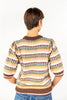 A woman shown from the back wearing a knit sweater with horizontal multicolor stripes in brown, cream, yellow, and light green.