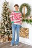 A woman wearing a festive red and white striped sweater with 'Love, Peace, Joy' written in red script and green trim, paired with blue jeans.