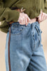 Close-up of a person wearing light blue drawstring jeans and an olive green knit cardigan, with hands pulling the hem up slightly.