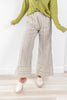 A person wearing wide-leg tan and blue striped pants with a green cardigan and white loafers, standing on a light wood floor against a white wall.