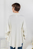 A woman viewed from the back wearing an oversized cream-colored ribbed knit top with blue jeans.