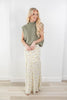 A woman modeling a sleeveless sage green mock neck knit top and a long cream maxi skirt with a small yellow and green floral print, standing in a bright room with light wood floors.