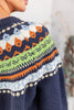 Close up of a navy blue knit sweater with a colorful Fair Isle yoke pattern in green, orange, white, and blue.