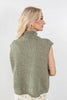 A woman shown from the back wearing a sleeveless ribbed knit mock neck sweater in a heathered sage green color, paired with a floral skirt, against a plain light gray background.