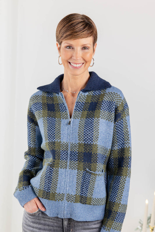 A woman wearing a blue and green plaid zip-up sweater jacket with a navy blue collar, paired with gray jeans.