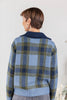 A woman shown from the back wearing a blue knit sweater with a plaid pattern in navy and olive green.