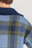Close-up of the back of a woman wearing a blue plaid knit sweater with a dark navy ribbed collar.