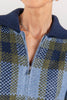 Close-up of a person wearing a zipper front knit sweater with a blue and olive plaid pattern and a navy ribbed collar.