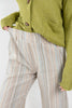 Close-up of a person wearing striped trousers with vertical stripes in beige, blue, and orange, paired with an olive green cardigan.