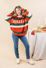 A woman modeling a festive striped sweater with 'GRATEFUL' written across the chest in white. The sweater features horizontal stripes of orange, green, and cream.