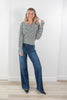 A woman modeling a black and white striped long-sleeve button-up cardigan with wide-leg blue jeans and black pointed-toe flats, standing against a white wall and light wood floor.