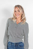 A smiling blonde woman wearing a long-sleeve black and white striped button-up cardigan tucked into blue jeans, photographed against a clean white studio background.