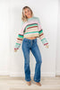 A woman modeling a pastel striped cropped knit sweater and blue jeans in a bright indoor setting with a white wall and light wood floor.