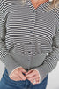 A close-up of a person wearing a black and white horizontally striped long-sleeve button-up cardigan with dark buttons, paired with blue jeans.