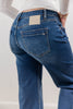 Close-up back rear view of a person wearing blue denim jeans with a white ribbed long-sleeve top. The jeans show a light beige Mica brand patch on the back waistband and a large back pockets.