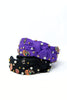 Two knotted fabric headbands stacked on a white background, one in purple and one in black, both decorated with small pumpkin charms, white faux pearls, and gold and silver rhinestones.