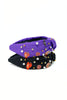 Two fabric headbands stacked on a white background, one purple and one black, both decorated with small halloween pins, white pearls, and gold and silver rhinestones.