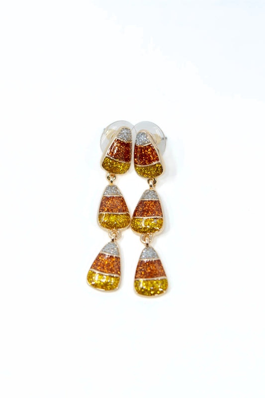 A pair of dangling earrings with a candy corn design, featuring textured orange, yellow, and white glitter sections in a gold-tone setting, shown against a plain white background.