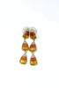 A pair of dangling earrings with a candy corn design, featuring textured orange, yellow, and white glitter sections in a gold-tone setting, shown against a plain white background.