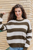 A woman wearing a brown and off-white horizontally striped waffle-knit sweater and halloween earrings, standing in front of a beige brick wall.