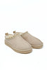 A pair of beige suede slip-on slippers with a decorative braided trim around the collar and a soft cream-colored shearling lining, shown on a plain white background.